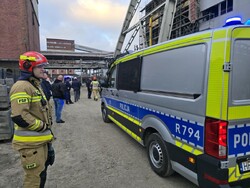 Obok radiowozu Policji stoi strażak w umundurowaniu