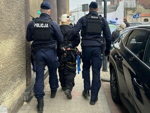 Policjanci umundurowani prowadzą chodnikiem osobę zatrzymaną