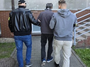 Policjanci nieumundurowani idą w kierunku schodów z zatrzymanym