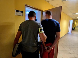 Policjant przeprowadza przez drzwi zatrzymanego