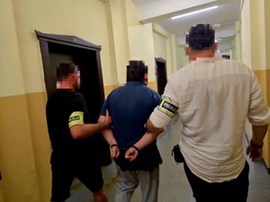 Zatrzymanego mężczyznę prowadzą korytarzem policjanci