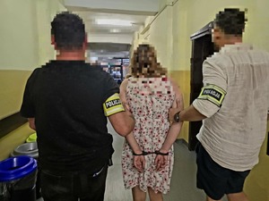 Korytarzem policjanci prowadzą zatrzymaną kobietę