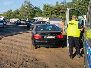 Policjanci wykonujący czynności na parkingu pojazdów przy jeziorze.