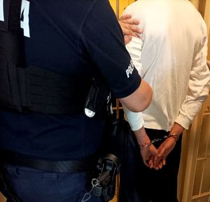 Zdjęcie policjanta oraz osoby zatrzymanej z założonymi kajdankami.