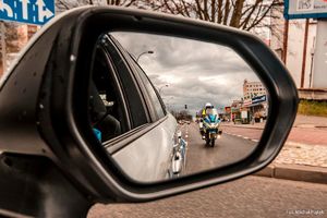 Zdjęcie przedstawiające policjanta na motocyklu widocznego w lusterku pojazdu.