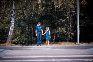 Zdjęcie przedstawiające policjantkę oraz dziewczynkę  przechodzącą przez przejście dla pieszych.
