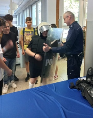 Zdjęcie przedstawiające uczniów klas ósmych oraz policjanta, który prezentuje sprzęt policyjny.