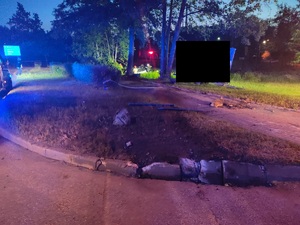 Zdjęcie przedstawiające uszkodzony krawężnik na skrzyżowaniu i rozbity samochód w oddali.