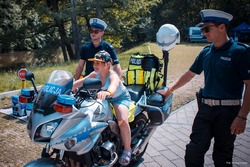 Zdjęcie przedstawiające dwóch policjantów ruchu drogowego oraz dziewczynka na motocyklu policyjnym.