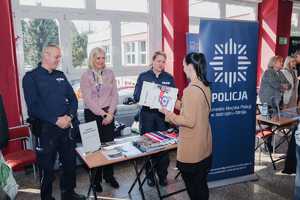 Zdjęcie przedstawiające policjantkę, policjanta, panią kadrową oraz osoby zainteresowane przy stoisku.