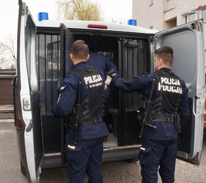 Zdjęcie dwóch policjantów, osoby zatrzymanej oraz radiowóz.