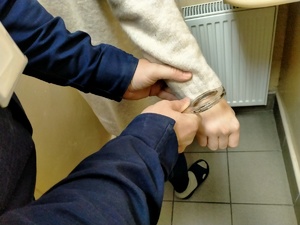 Zdjęcie policjanta zakładającego kajdanki.