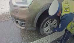 Zdjęcie policjanta ruchu drogowego wymieniającego koło w pojeździe.