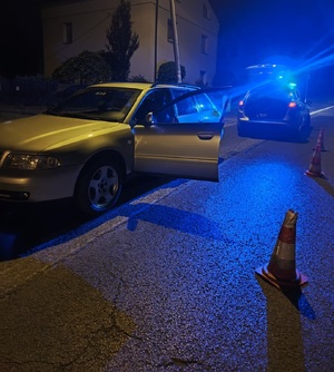 Zdjęcie policyjnego radiowozu z włączonymi sygnałami oraz samochód audi.