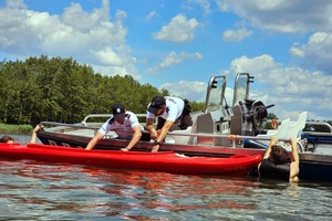 dwóch umundurowanych policjantów będących na łodzi służbowej przytrzymują kajak, obok dwóch mężczyzn w wodzie