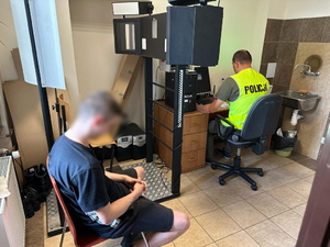 na zdjęciu zatrzymany mężczyzna siedzący na krześle w pokoju technika kryminalistyki, który rejestruje dane na komputerze