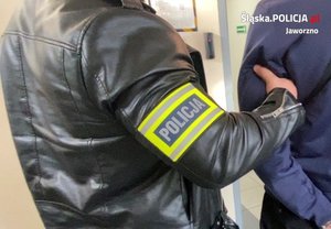 nieumundurowany policjant w opasce na napisem policja trzyma zatrzymanego