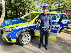 na zdjęciu umundurowany policjant stojący przy policyjnym radiowozie, trzymający kluczyk
