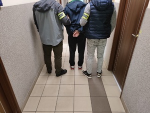 na zdjęciu dwóch nieumundurowanych policjantów trzymających mężczyznę w kajdanckach