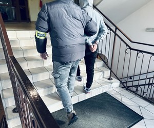 na zdjęciu nieumundurowany policjant prowadzi zatrzymanego mężczyznę