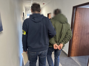 na zdjęciu nieumundurowany policjant trzyma zatrzymanego mężczyznę w kajdankach