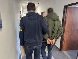 na zdjęciu nieumundurowany policjant trzyma zatrzymanego mężczyznę w kajdankach