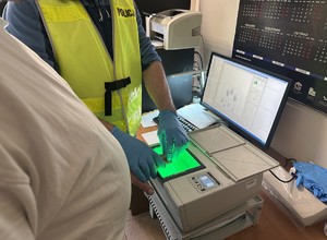 na zdjęciu technik kryminalistyki wykonuje daktyloskopię zatrzymanemu mężczyźnie