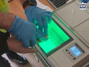 na zdjęciu technik kryminalistyki wykonuje daktyloskopię zatrzymanemu mężczyźnie