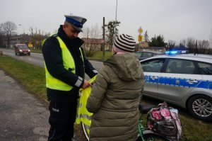 Policjant wręcza kamizelkę odblaskową.