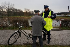 Policjant wręcza kamizelkę odblaskową.