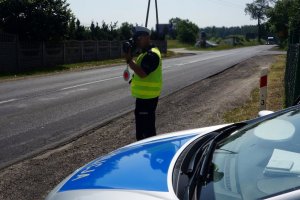 policjant stoi przy drodze i kontroluje prędkość