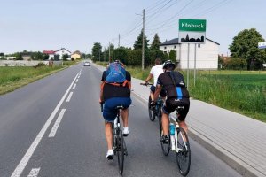 rowerzyści jadący jezdnią, w tle znak miejscowości Kłobuck