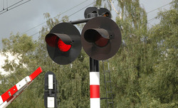 Zdjęcie przedstawia czerwone światło na sygnalizatorze na przejeździe kolejowym.