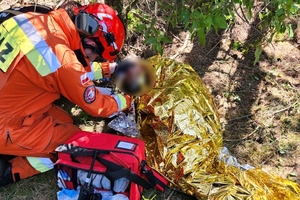 Zdjęcie przedstawia strażaka udzielającego pomocy przedmedycznej leżącej na ziemi i przykrytej folią kobiecie.