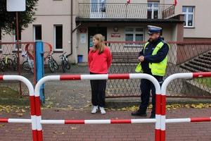 uczennica stoi przed budynkiem szkoły wraz z umundurowanym policjantem