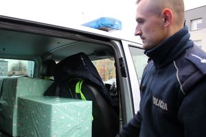 Zdjęcie przedstawia policjanta pakującego paczki do radiowozu.