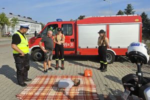 Zdjęcie przedstawia policjanta, strażaków ochotników, mężczyznę oraz policyjny motocykl i wóz strażacki.