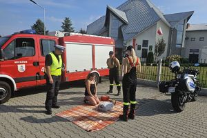 Zdjęcie przedstawia policjanta, strażaków ochotników, kobietę przy fantomie.