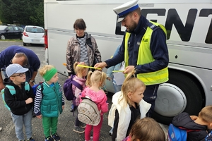 Zdjęcie przedstawia policjanta rozdającego opaski odblaskowe dzieciom.