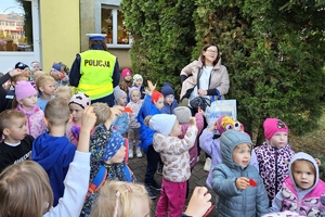 Zdjęcie przedstawia policjantkę rozdającą odblaski przedszkolakom.