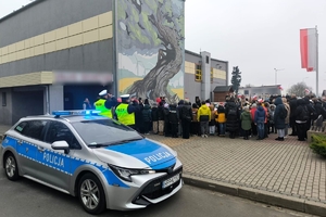 Zdjęcie przedstawia policjantów, radiowóz i uczestników wydarzenia w pozycji na baczność.