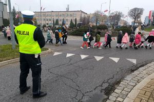 Zdjęcie przedstawia policjanta na drodze oraz uczestników wydarzenia podczas tańca.