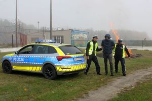 Zdjęcie przedstawia policjantów prowadzących zatrzymanego oraz radiowóz.