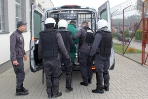 Zdjęcie przedstawia funkcjonariuszy służby więziennej transportujących zatrzymanego.