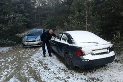 Zdjęcie przedstawia radiowóz oraz policjanta zerkającego przez szybę do pojazdu osobowego.