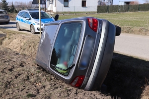 samochód renault w rowie, przewrócony na lewy bok, z tyłu dwa oznakowane policyjne radiowozy