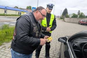 Zdjęcie przedstawia policjanta oraz motocyklistę przekazujących naklejkę kierowcy.