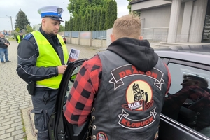 Zdjęcie przedstawia policjanta oraz motocyklistę przekazujących naklejkę kierowcy.