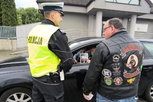 Zdjęcie przedstawia policjanta oraz motocyklistę przekazujących naklejkę kierowcy.