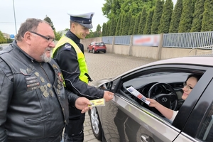 Zdjęcie przedstawia policjanta oraz motocyklistę przekazujących naklejkę kierowcy.